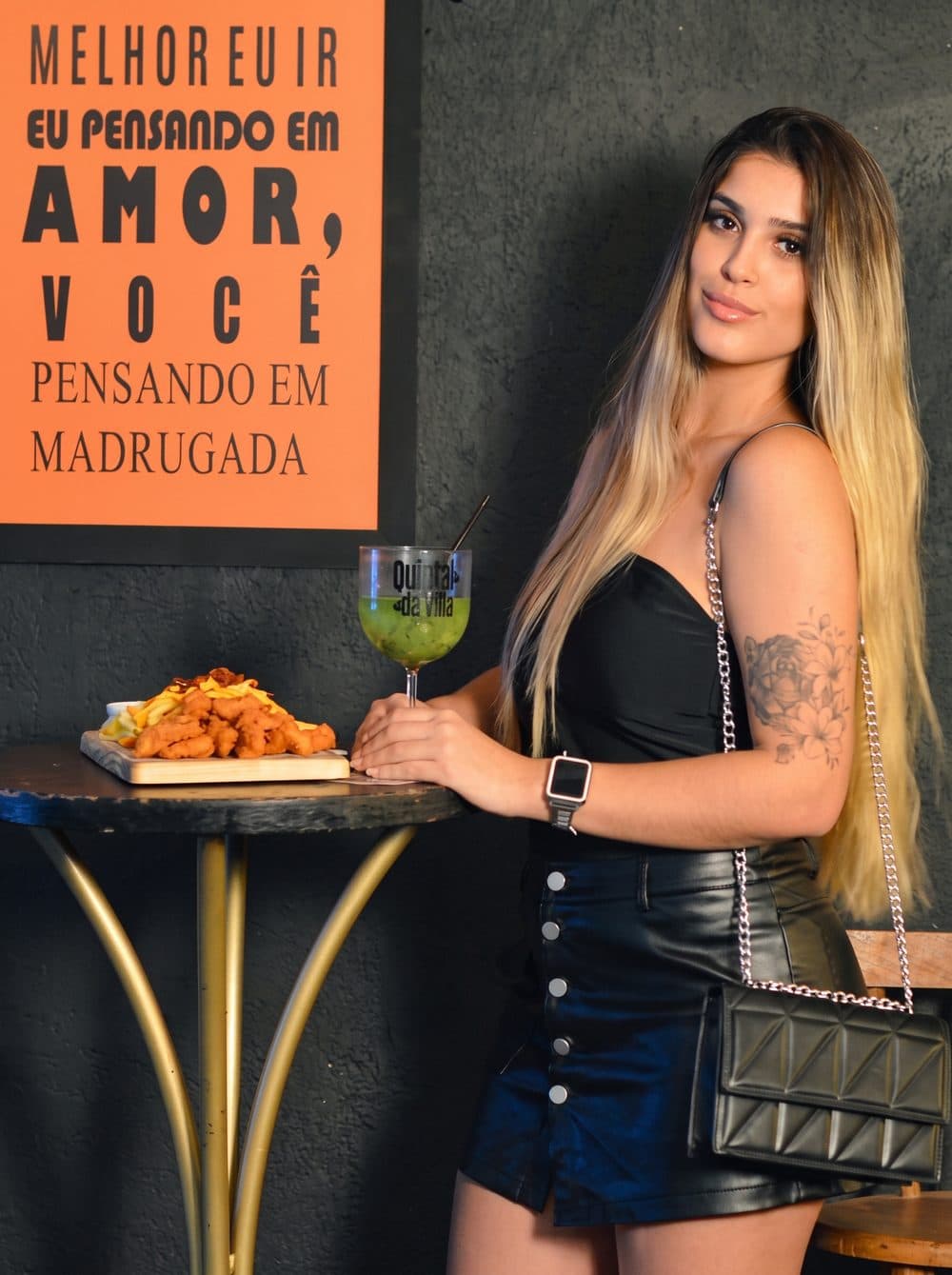 Mesa com porção e drink servido no copo da casa, ambiente do Quintal da Villa